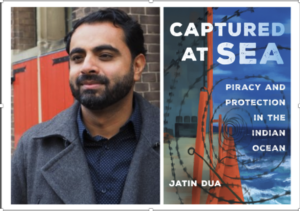 A person with a beard, wearing a gray coat, stands in front of a brick building with red doors. Next to the person is the book cover of "Captured at Sea: Piracy and Protection in the Indian Ocean" by Jatin Dua, featuring ocean waves and barbed wire.